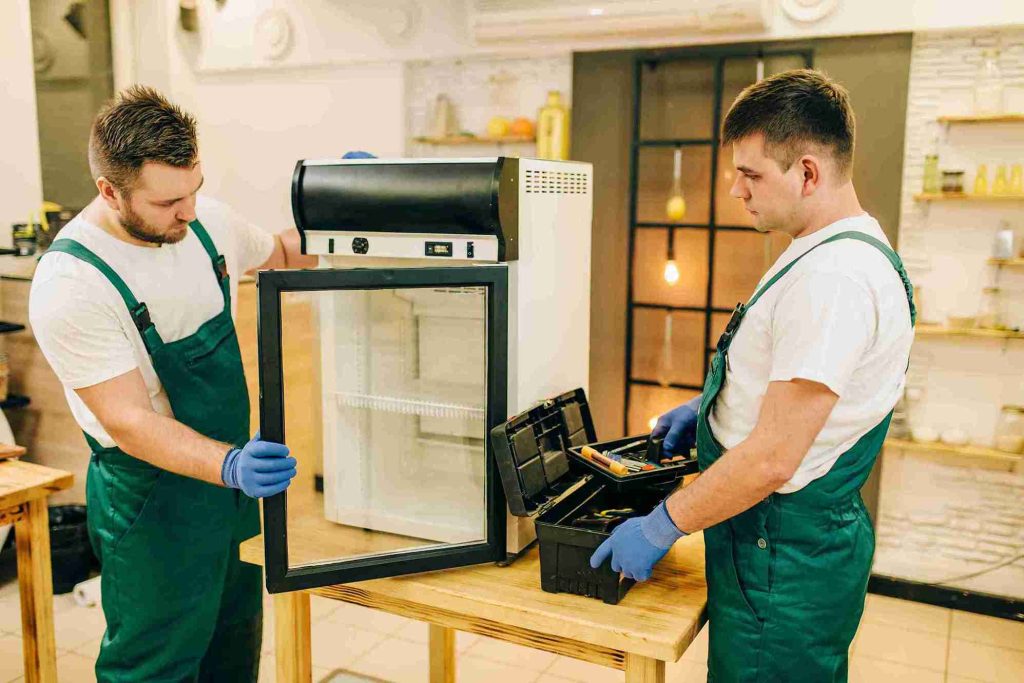 two-workers-in-uniform-repair-refrigerator-at-home-2023-11-27-05-31-18-utc_11zon